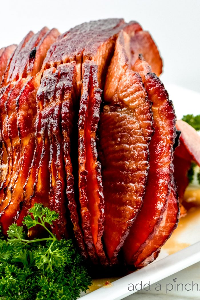 Cola Glazed Ham Recipe 
 on serving platter with garnish - addapinch.com