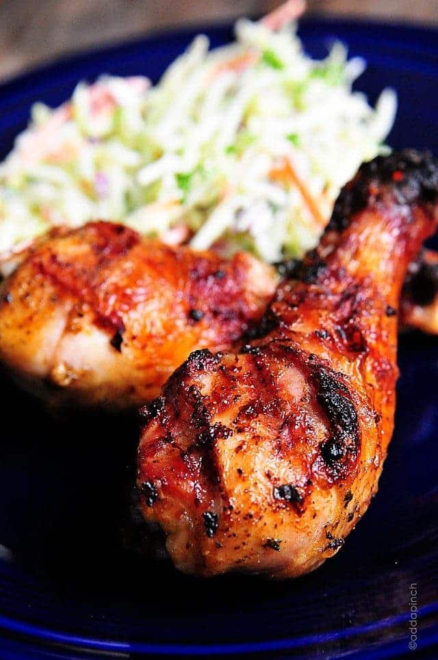 Grilled chicken legs using chicken marinade are sitting on a blue plate beside coleslaw.