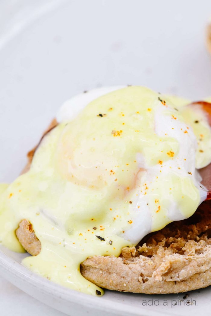 Toasted English muffins topped with Canadian bacon and poached eggs and drizzled with hollandaise sauce, all on a white plate. 