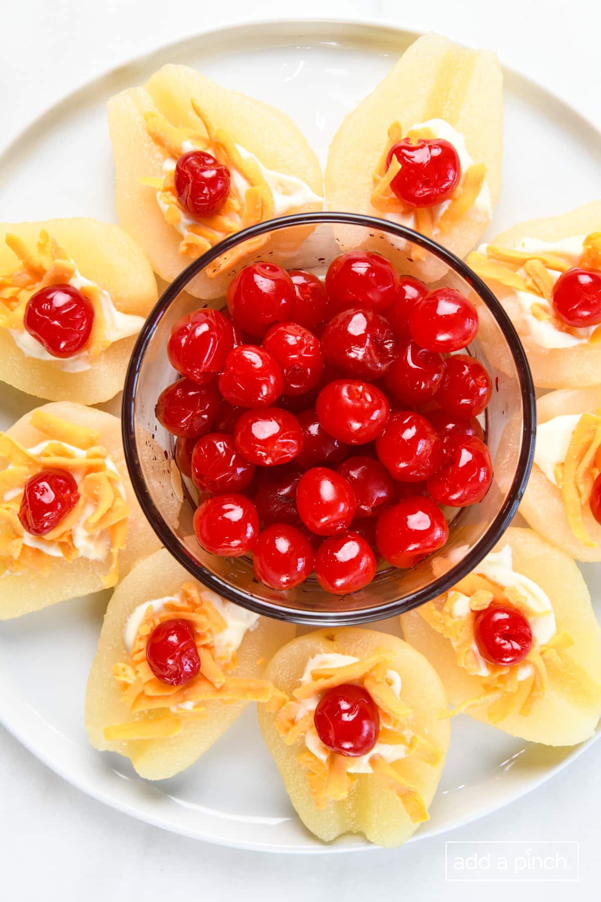 Photo of pears topped with cheese and cherries and a bowl of cherries on a white platter.