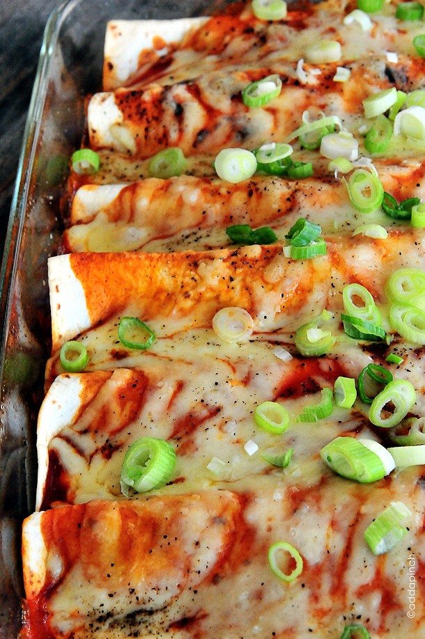 Glass baking dish filled with enchiladas topped with melted cheese and enchilada sauce and garnished with green onion 