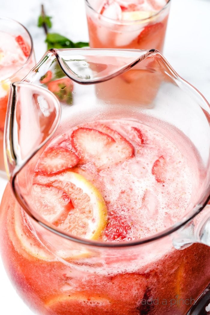 Glass pitcher and glasses of strawberry lemonade garnished with fresh strawberries and lemon slices // addapinch.com