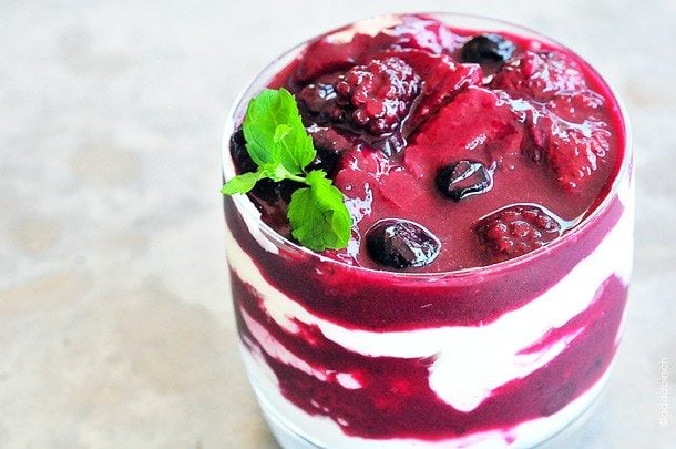 Image of glass filled with greek yogurt layers with a berry sauce and topped with mint. // addapinch.com