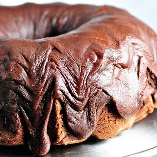 Photo of chocolate pound cake with fudge icing on a silver cake stand.