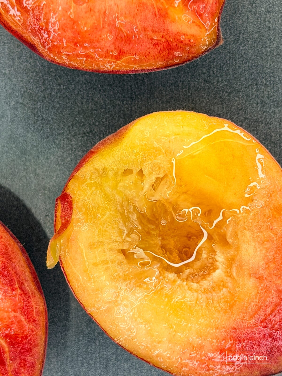 Roasted fresh peaches drizzled with maple syrup on a baking sheet for homemade peach ice cream.