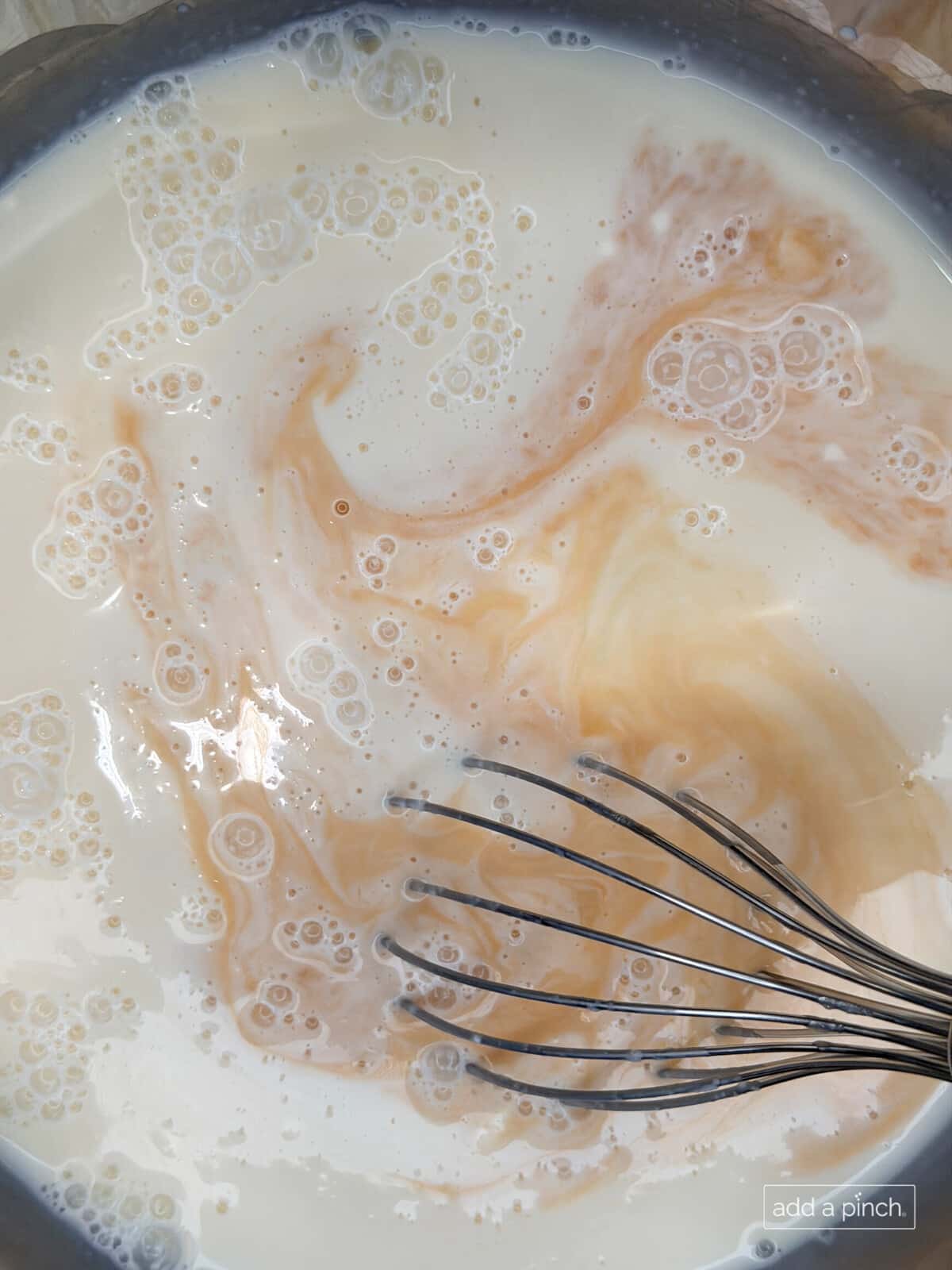 Whisking together whole milk, heavy whipping cream, sugar, maple syrup, and vanilla in a large bowl to create the smooth base for this easy homemade peach ice cream recipe