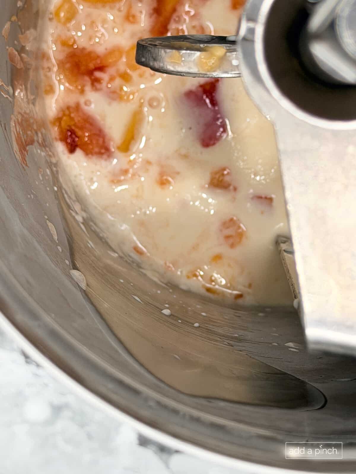 Roasted peaches added to ice cream base in ice cream maker to make easy homemade peach ice cream