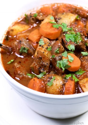 Photograph of homemade beef stew in a white bowl on a white background. // addapinch.com