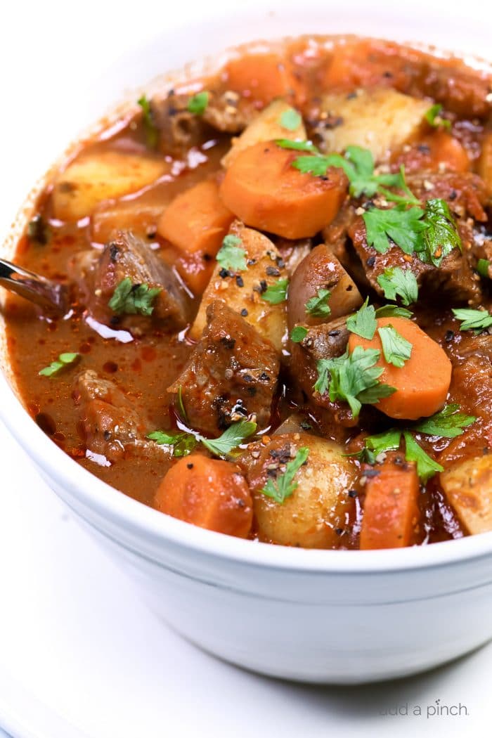 Photograph of homemade beef stew in a white bowl on a white background. // addapinch.com