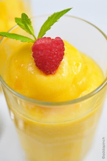 Frozen Peach Sorbet in a glass topped with fresh ripe raspberry and a sprig of mint on a white background.