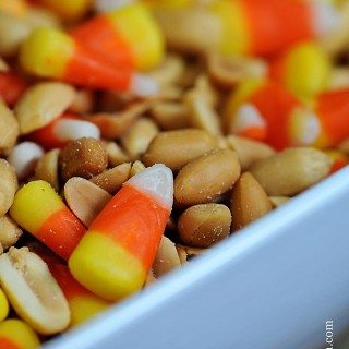 Candy corn mixed with coctail peanuts in white bowl.