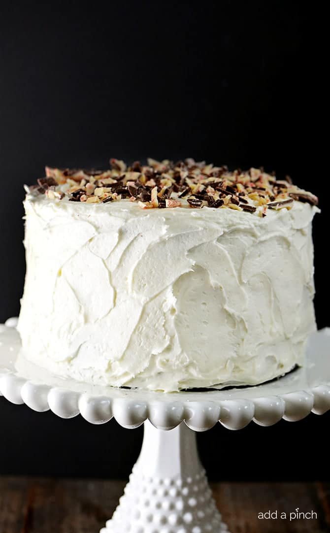 Peppermint Buttercream frosting on Chocolate Cake, topped with Peppermint Bark crumbles, on a white cake plate