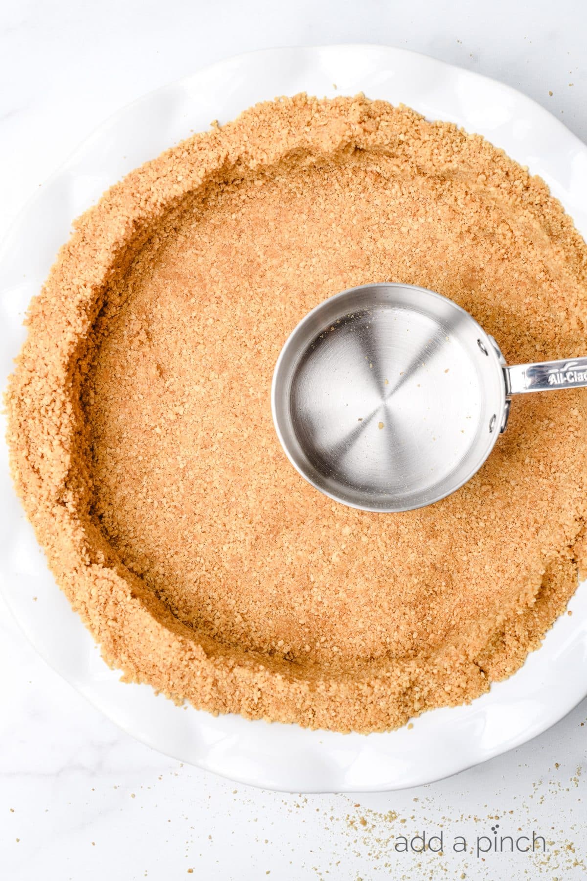 Graham cracker crust is formed into a pie plate with a dry measuring cup used to press crust together.