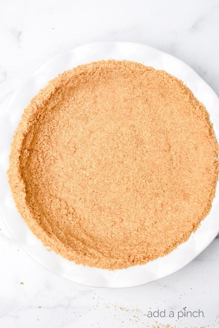 Graham cracker crust in a white pie plate on a marble surface.