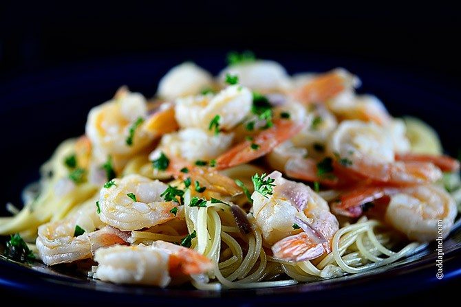Side view of cooked shrimp over pasta, served on dark plate  // addapinch.com
