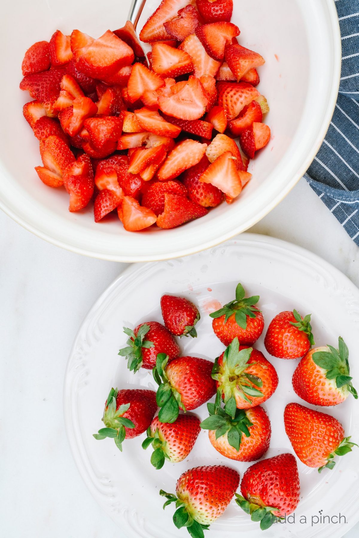 Photograph of strawberries on a white plate and sliced strawberries in a white bowl on a white marble background. // addapinch.com