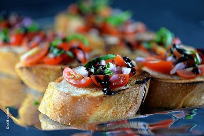 Bruschetta with tomato-basil topping and a drizzle of balsamic glaze on a silver tray.