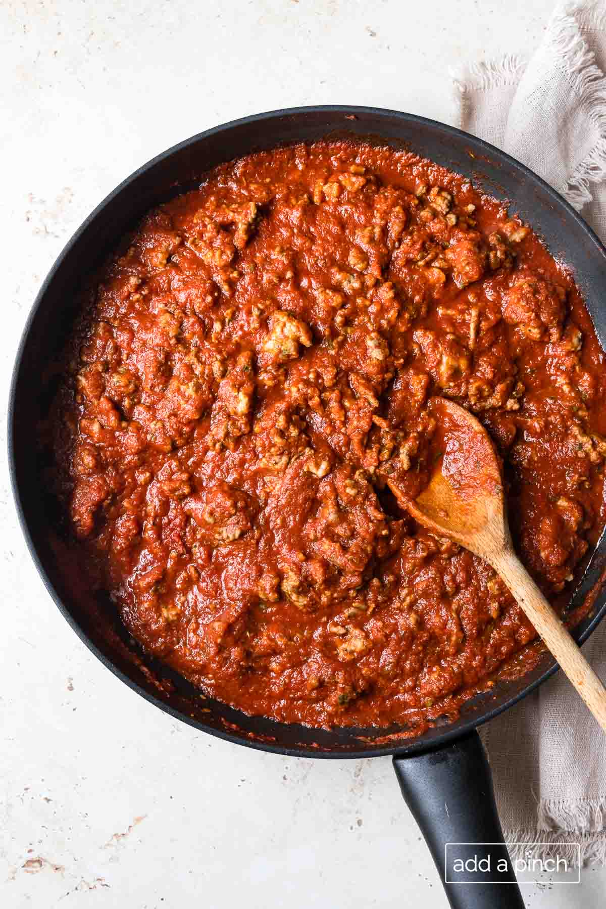 Photograph of lasagna meat sauce in a skillet with a wooden spoon. 
