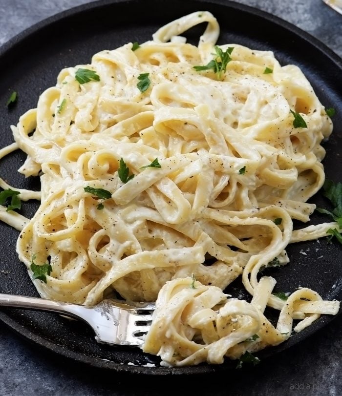 Black plate with Fettuccine covered with Alfredo sauce // addapinch.com