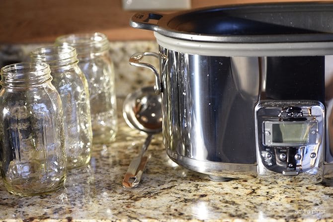 Slow cooker, canning jars, and ladle on a quartz countertop.