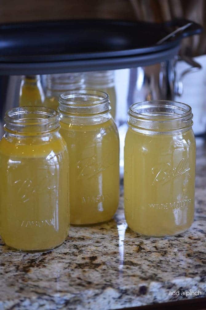 Three ball canning jars filled with homemade chicken stock on a quartz countertop with a slow cooker in the background.