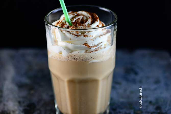 Pumpkin Spice Latte in clear glass topped with swirled whipped cream and pumpkin spice. // addapinch.com