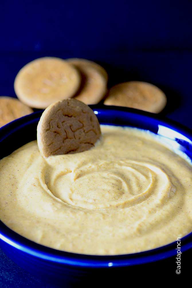 Image of pumpkin cheesecake dip in a blue bowl with a gingersnap cookie used for dipping. // addapinch.com