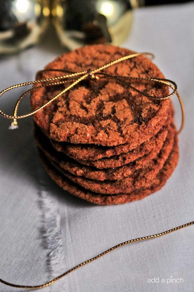 A stack of ginger molasses cookies are tied with golden twine and served on a white napkin. 