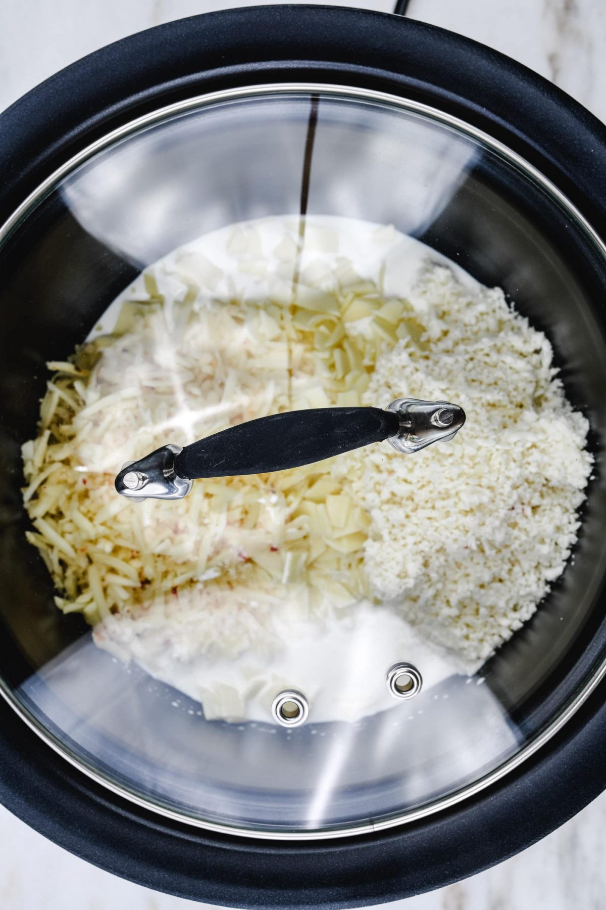 All ingredients for queso are added to a slow cooker with a glass lid.