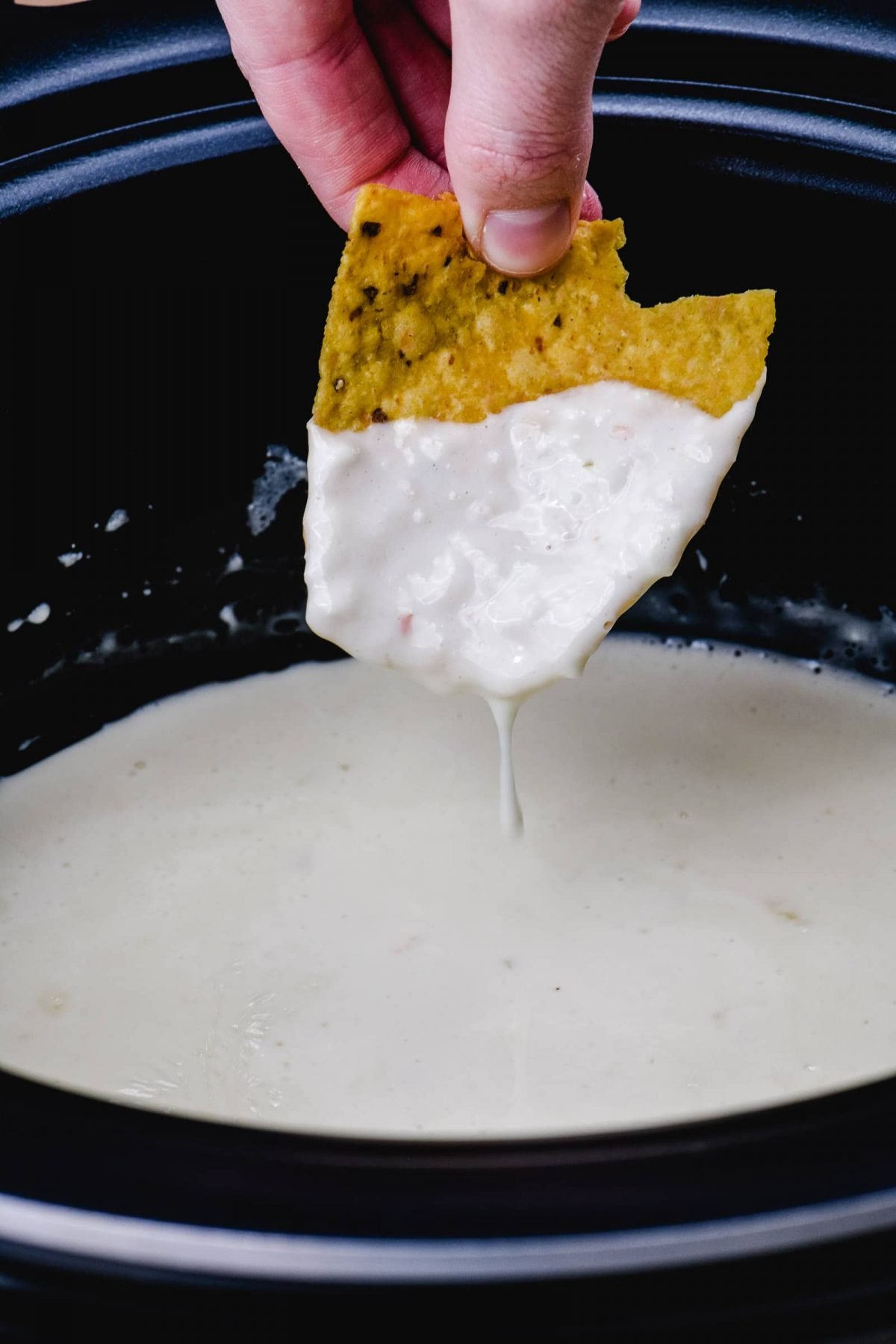 Tortilla chip dips into queso in a slow cooker. 