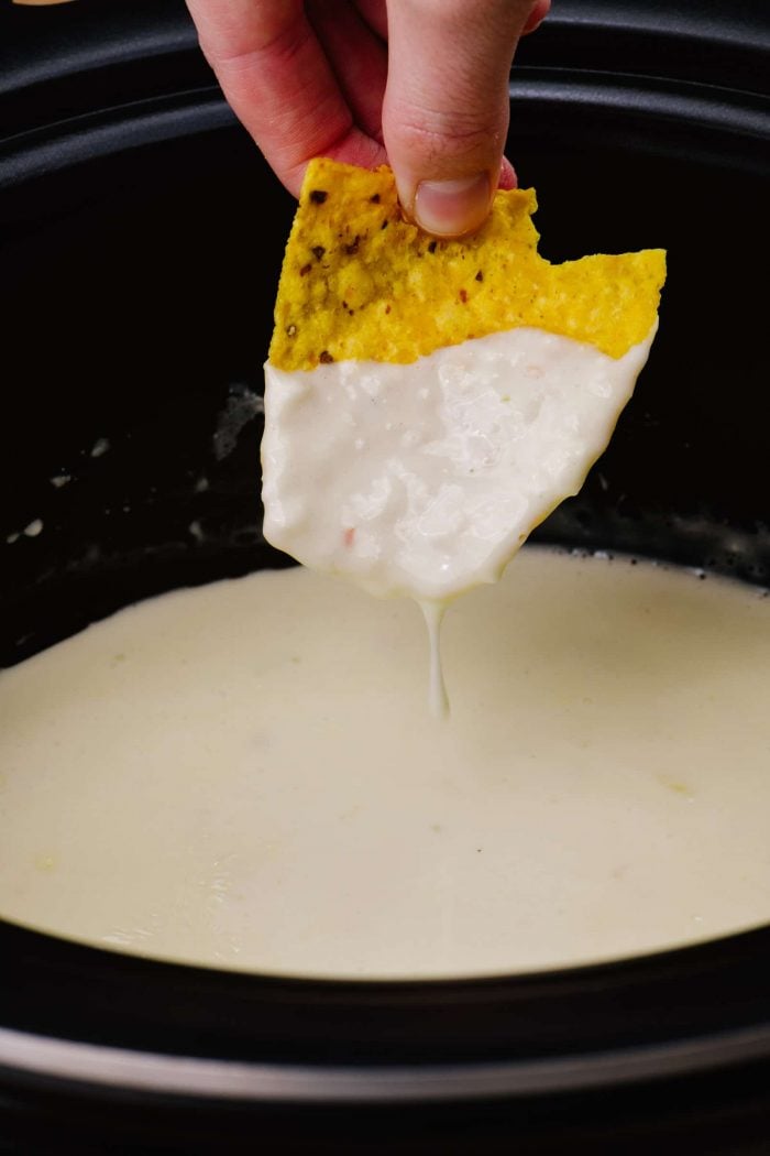 Slow cooker full of queso cheese dip, also being dipped on a tortilla chip