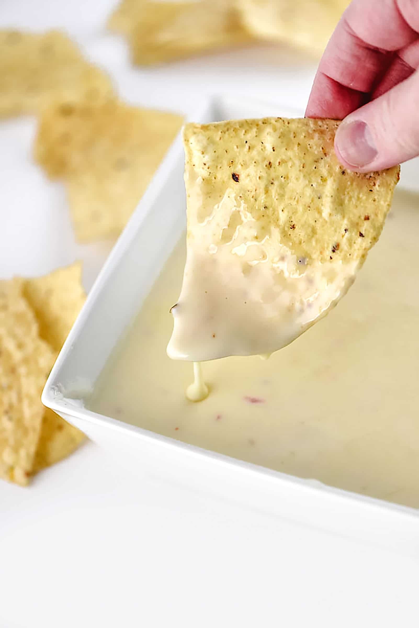 Creamy cheesy Queso Dip in white bowl is dipped with a tortilla chip.  