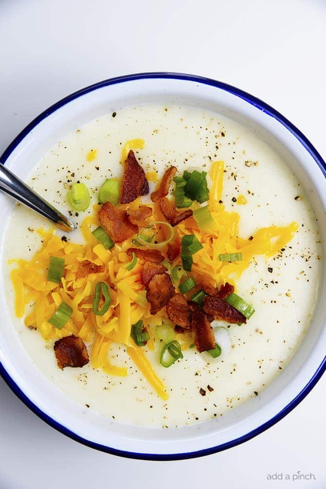 Potato soup in a white and blue rimmed enamel bowl, topped with shredded cheese, onions, and bacon // addapinch.com