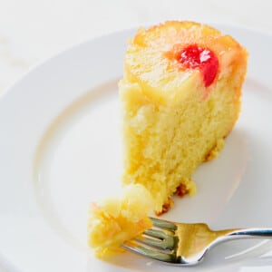 Slice of pineapple upside down cake on a white plate with a fork.
