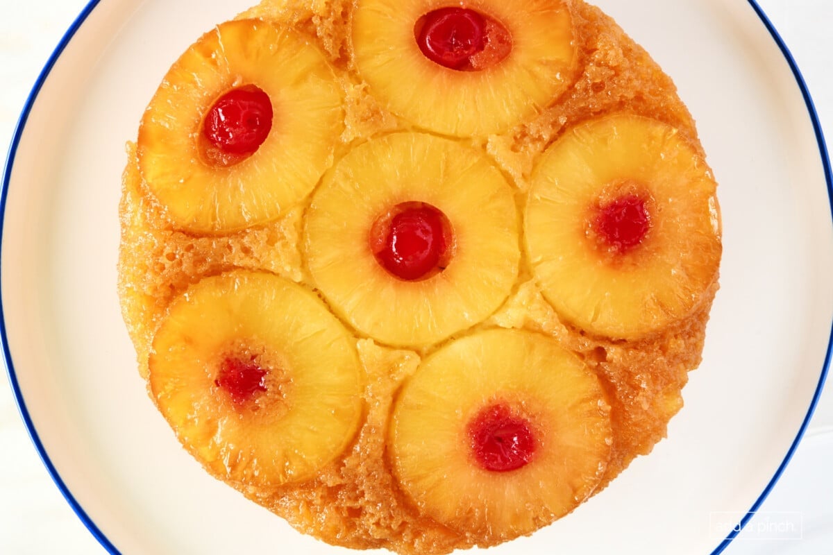 Pineapple upside down cake on a white cake stand with a blue rim on a marble surface.