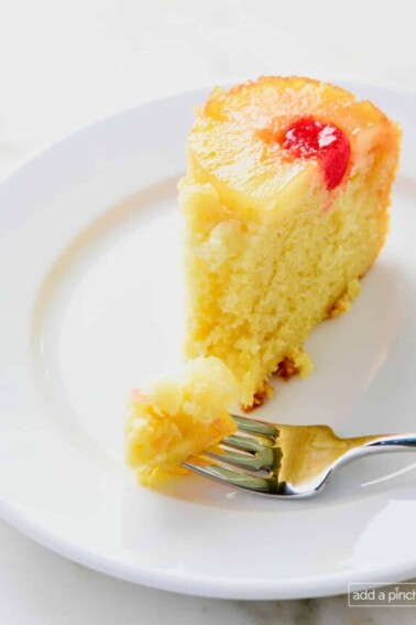 Slice of pineapple upside down cake on a white plate with a fork.