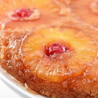 Pineapple upside down cake with pineapple and cherries on top on a white cake stand.