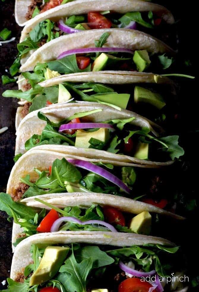 Colorful soft shell tacos filled with meat, lettuce, avocado, onion and tomatoes. 