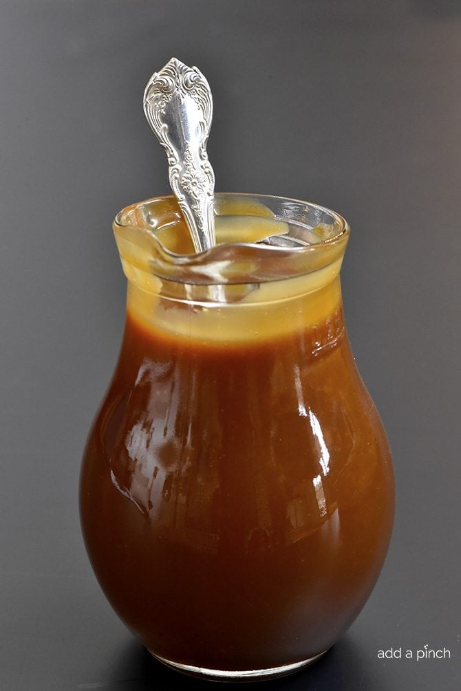 Glass pitcher with creamy salted Caramel Sauce and a silver spoon. 