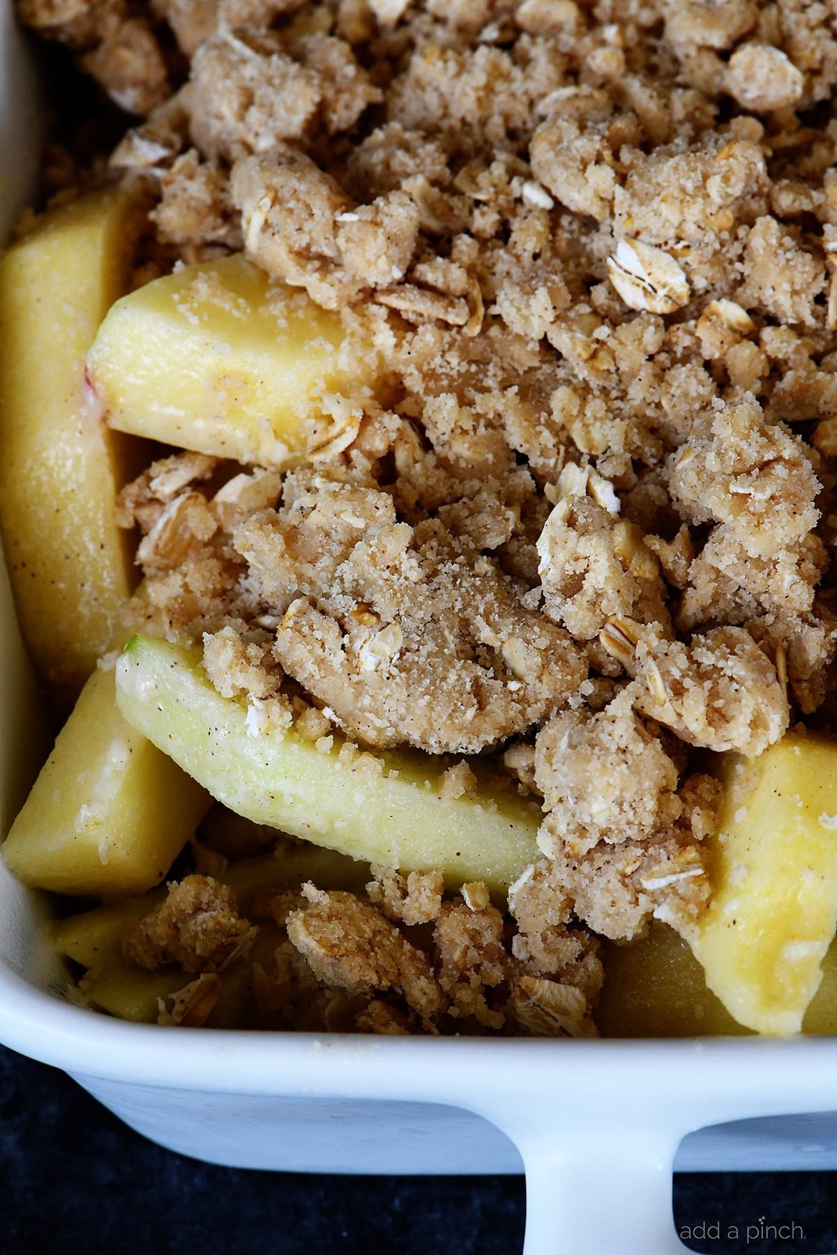 Apple filling is topped with oat streusel topping in white baking dish ready to bake. 