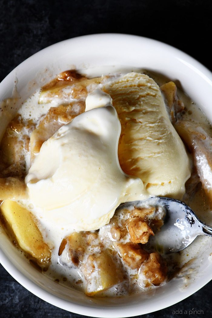 Bowl of Apple Crisp topped with ice cream being lifted with spoon.