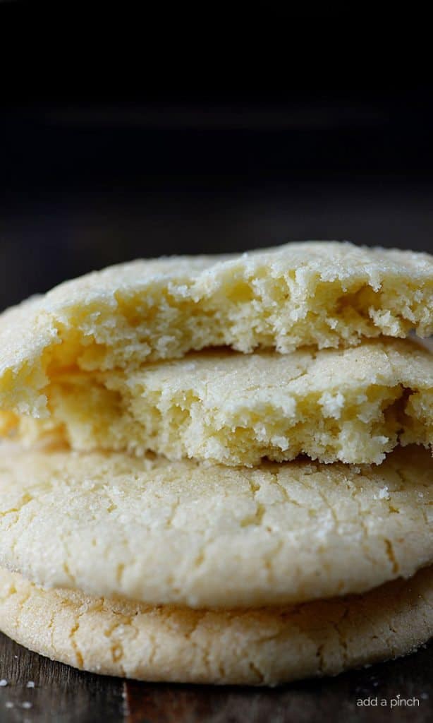 Close up photo of stack of Chewy Sugar Cookies with top cookie broken to show soft crumb and texture. On wooden board. 