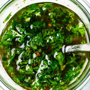 Fresh chimichurri sauce in a glass bowl with a spoon.
