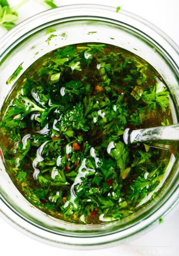 Fresh chimichurri sauce in a glass bowl with a spoon.