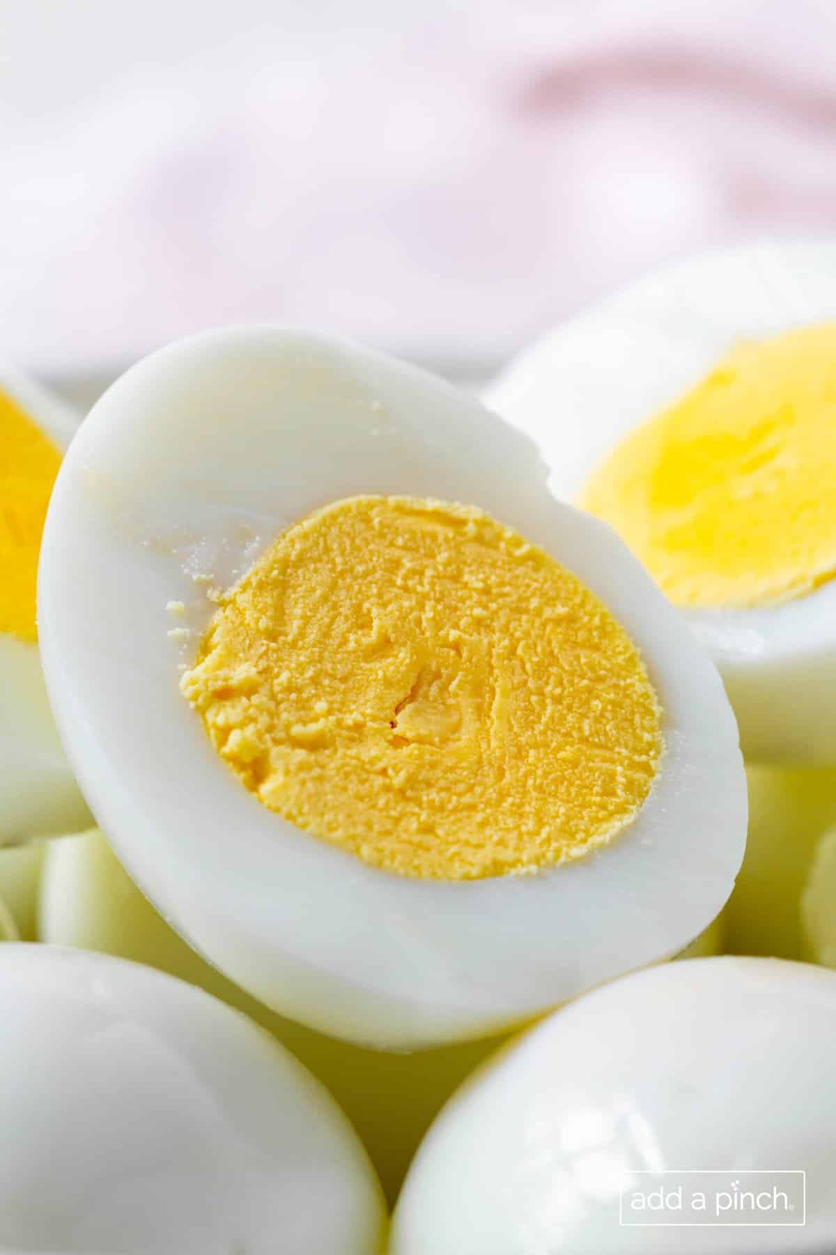 Bowl full of hardboiled eggs, eith some sliced in half with yolk visible. 