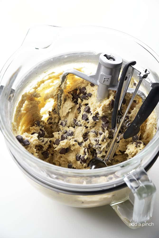 Photograph of chocolate chip cookie dough in a glass mixing bowl on white background. 