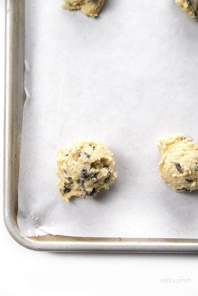Photograph of scoops of chocolate chip cookie dough on a baking sheet on a white background. 