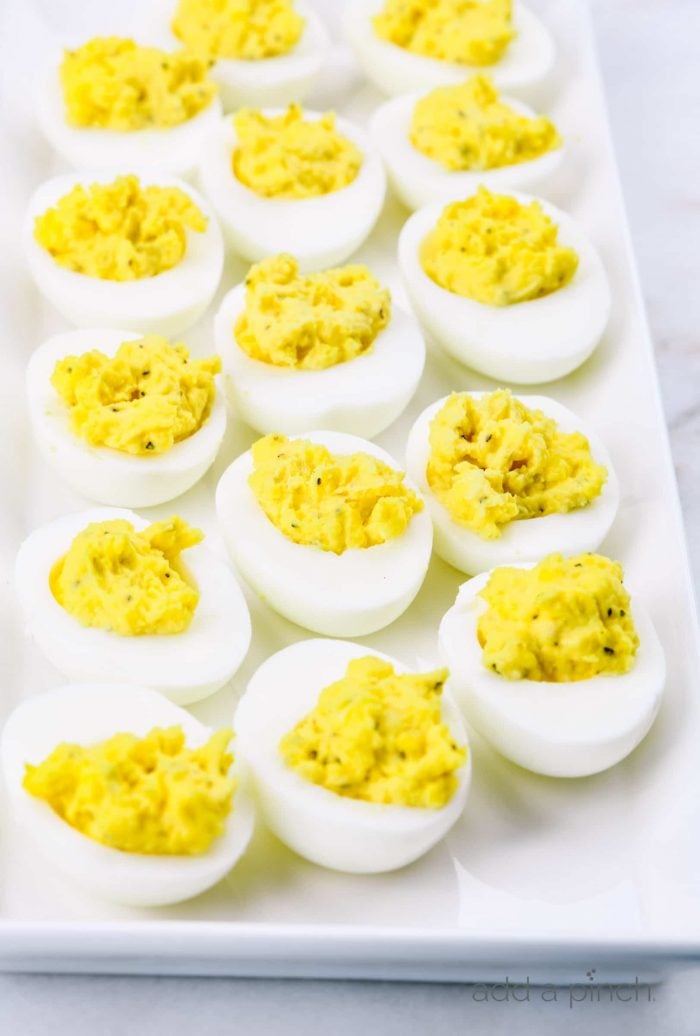 Photograph of deviled eggs on a white platter on a marble countertop.