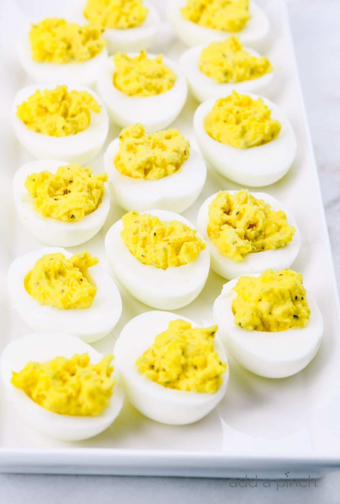 Photograph of deviled eggs on a white platter on a marble countertop.