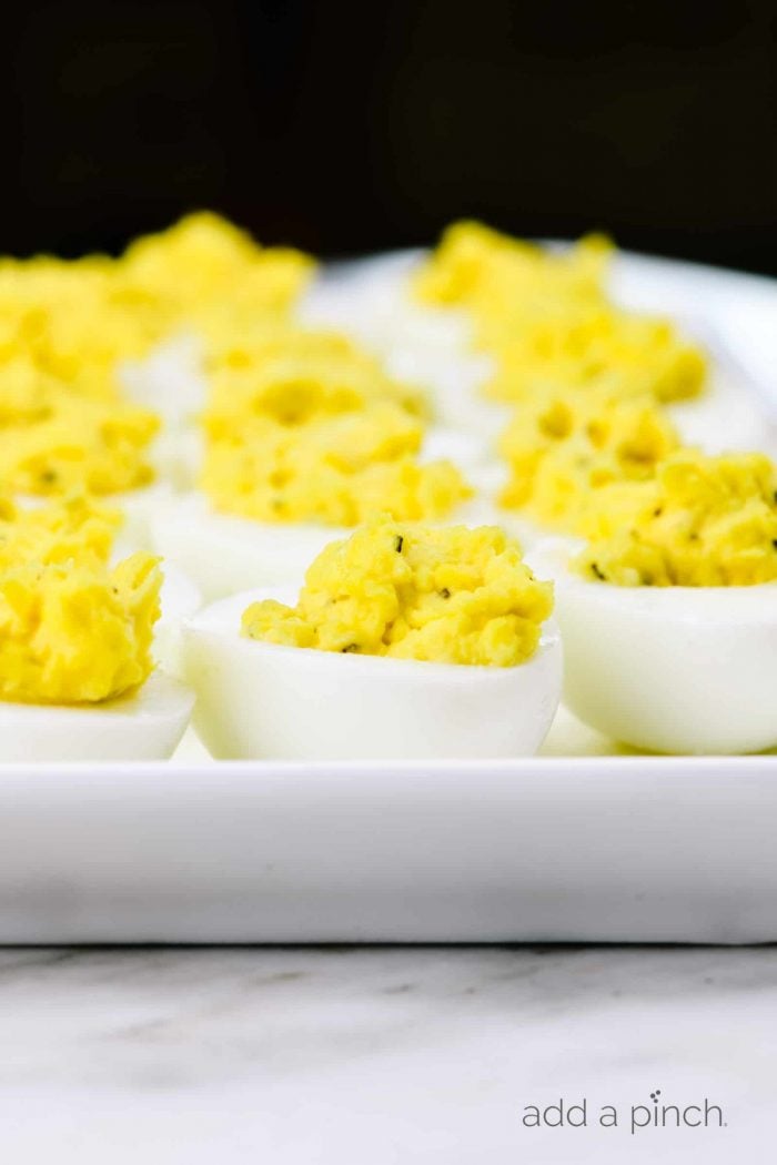 Photograph of hard boiled eggs that are stuffed on a white platter with black background